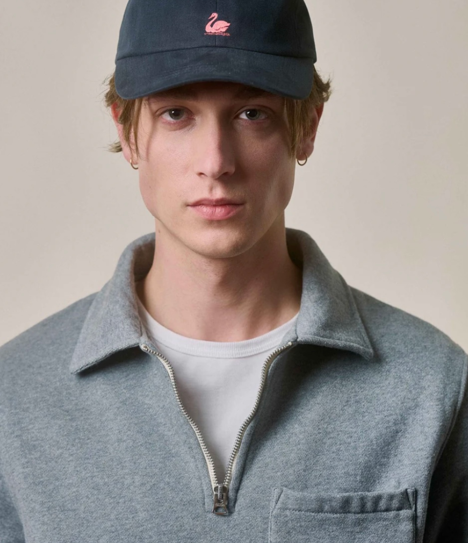 Person wearing a navy cap with a pink logo and a gray vest over a white shirt.
