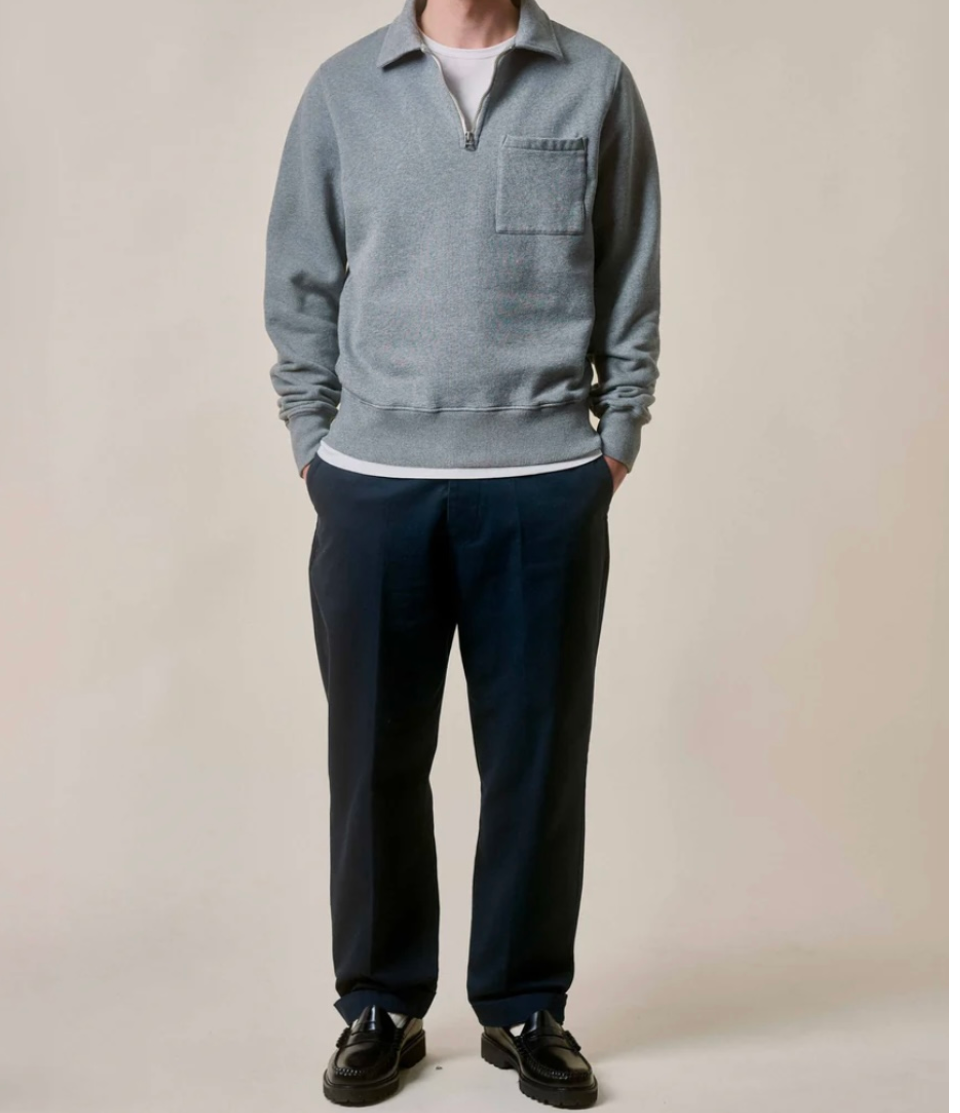 Person wearing a gray sweater and navy pants on a plain background