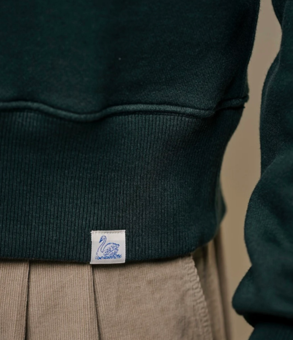 Dark green sweater with a brand label featuring a swan design on a beige background