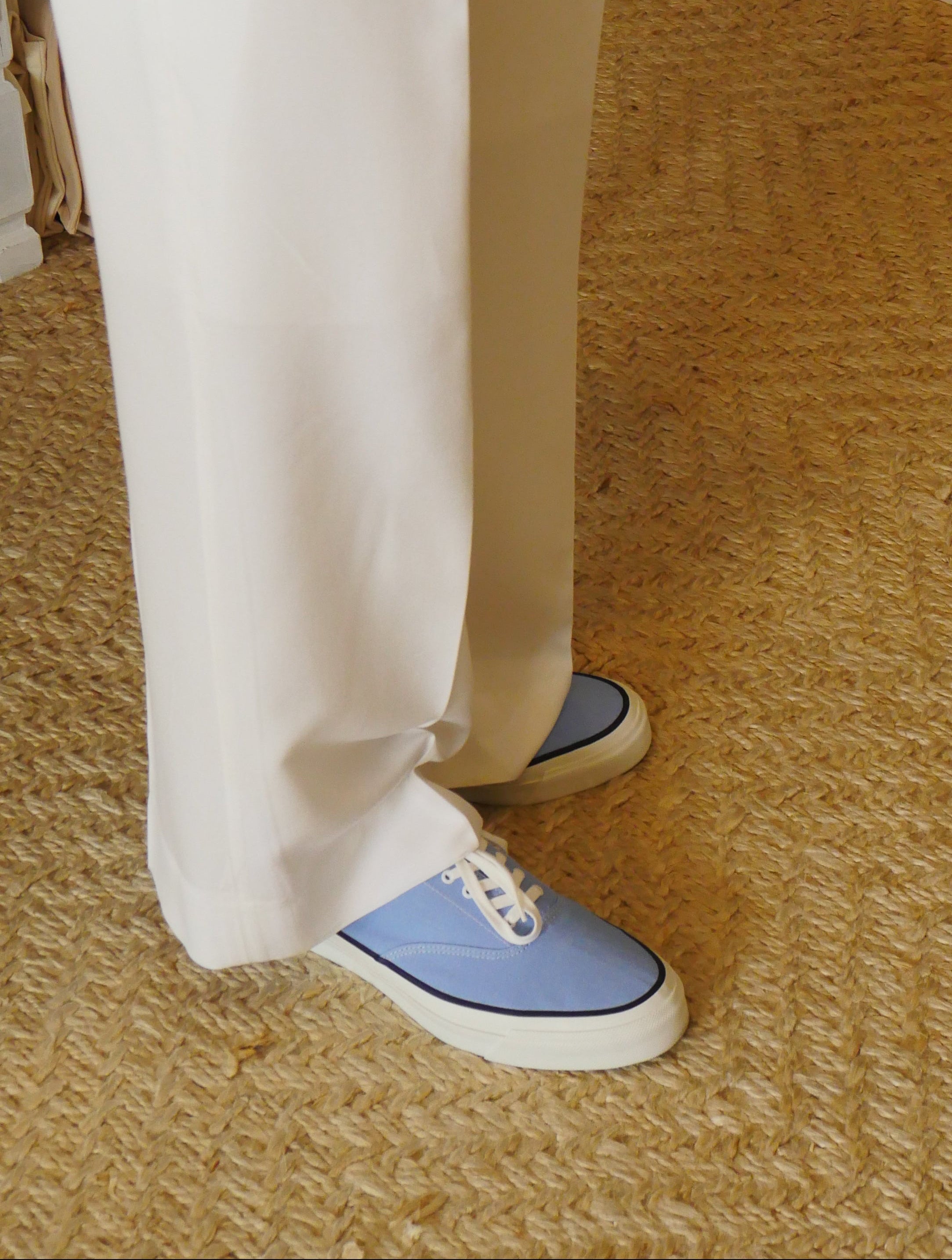 Person wearing white pants and blue sneakers on a carpeted floor.