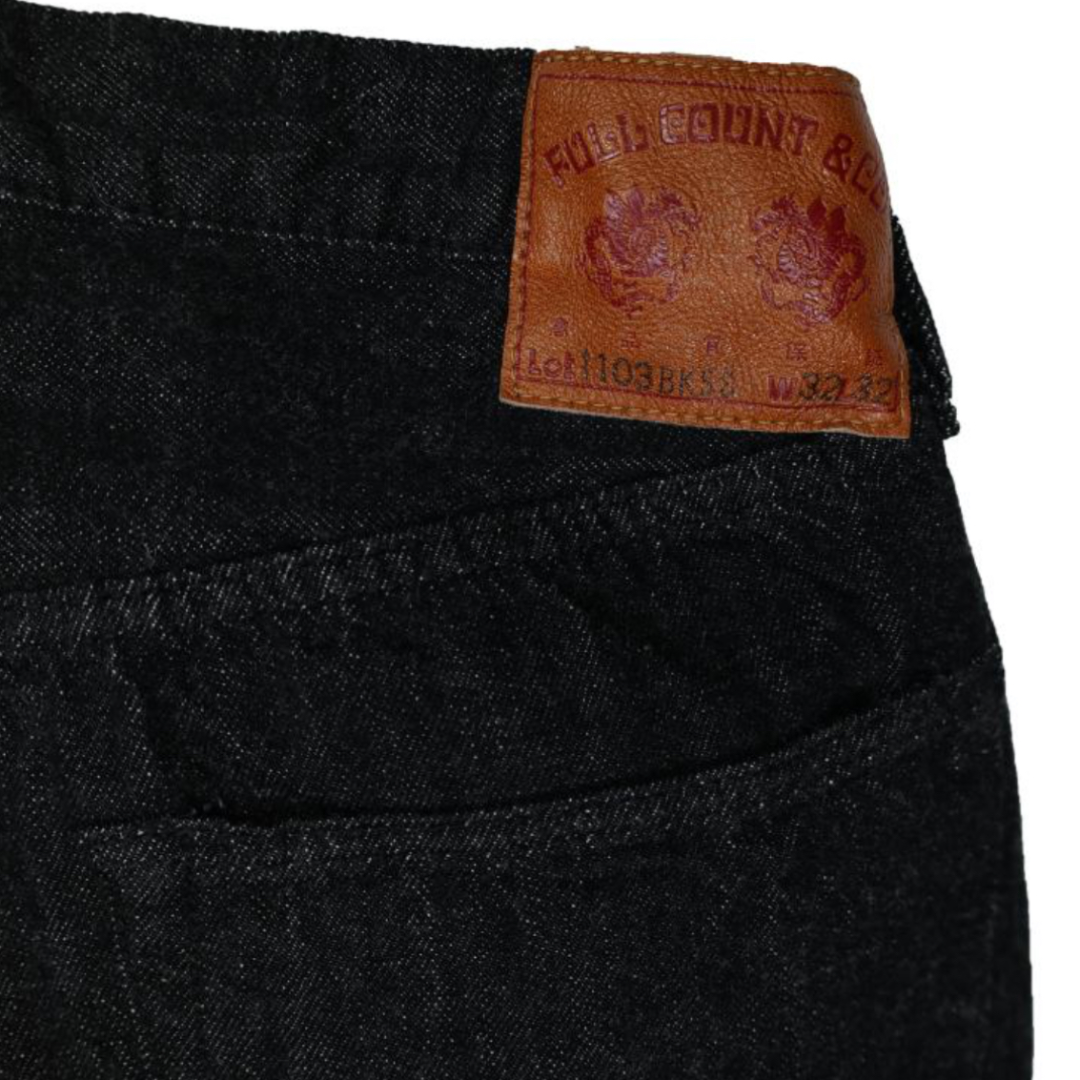 Close-up of a black denim fabric with a brown leather label featuring text and logos.