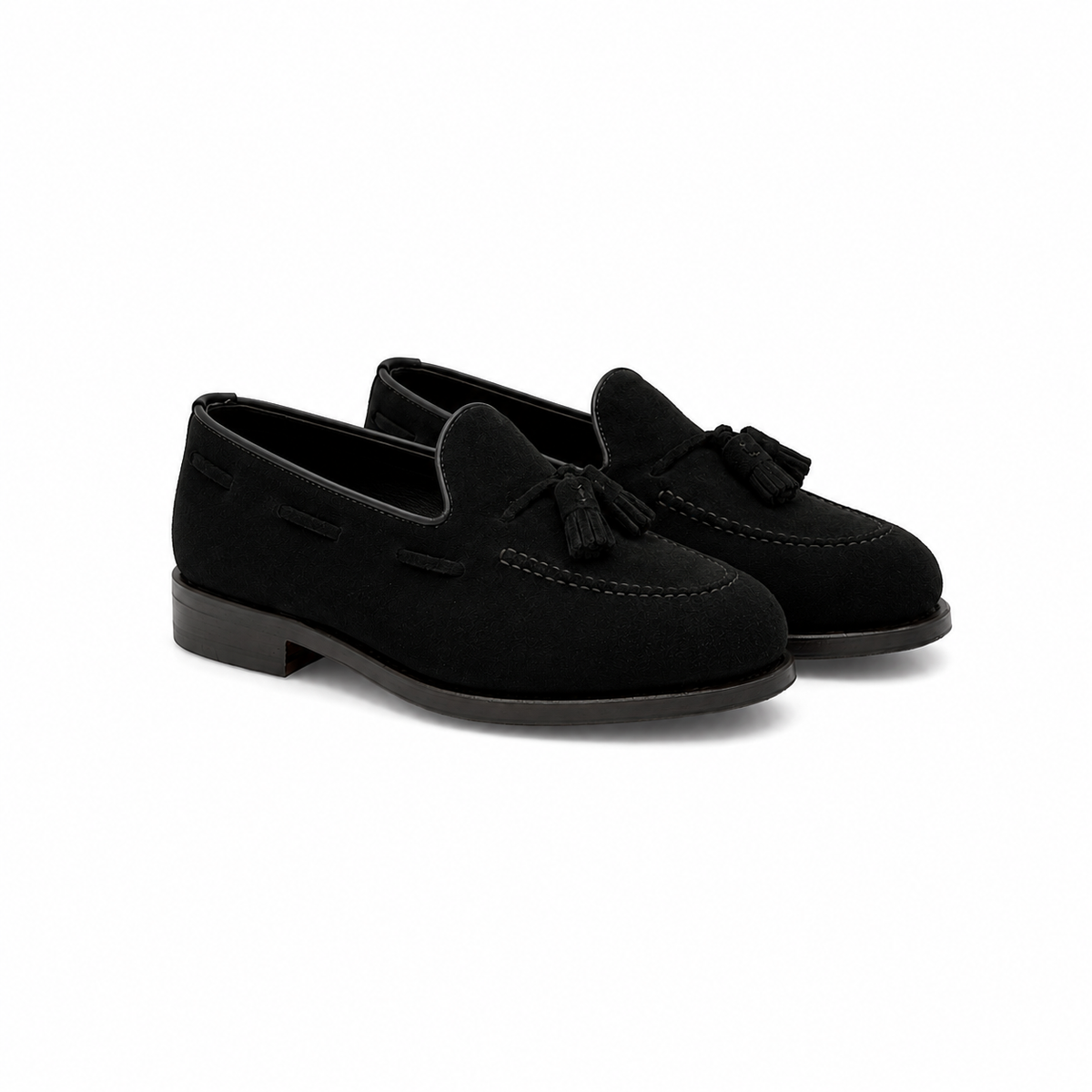 A pair of black suede tassel loafers with low block heels, shown from a three-quarters angle on a white background.