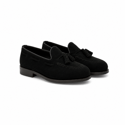 A pair of black suede tassel loafers with low block heels, shown from a three-quarters angle on a white background.