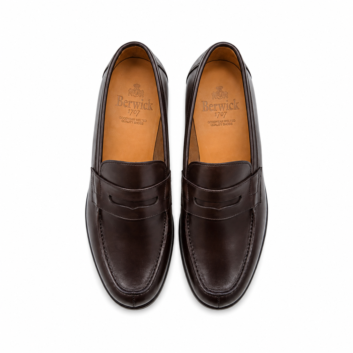 A pair of dark brown leather penny loafers shown from a top-down view on a clean white background. The brand name 'Berwick' is clearly visible on the tan insoles.
