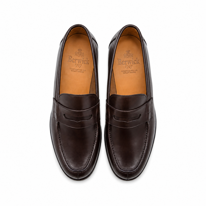 A pair of dark brown leather penny loafers shown from a top-down view on a clean white background. The brand name 'Berwick' is clearly visible on the tan insoles.
