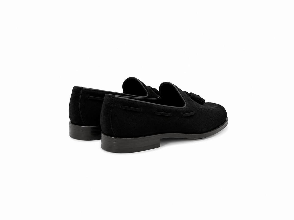 A pair of black suede tassel loafers shown from a three-quarters rear angle on a clean white background.