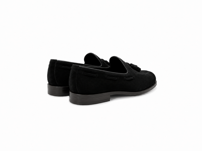 A pair of black suede tassel loafers shown from a three-quarters rear angle on a clean white background.