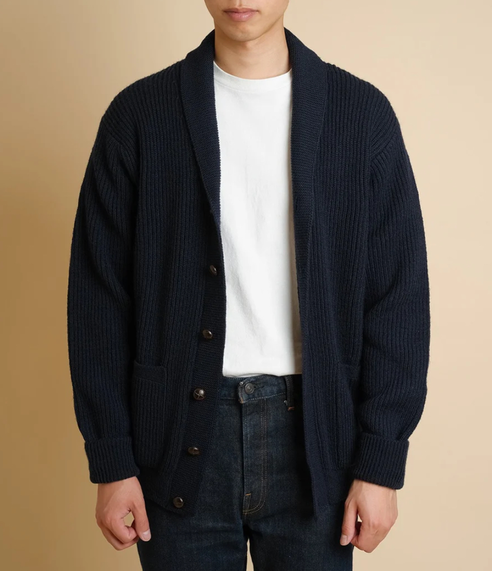 Person wearing a dark blue cardigan over a white shirt with a beige background