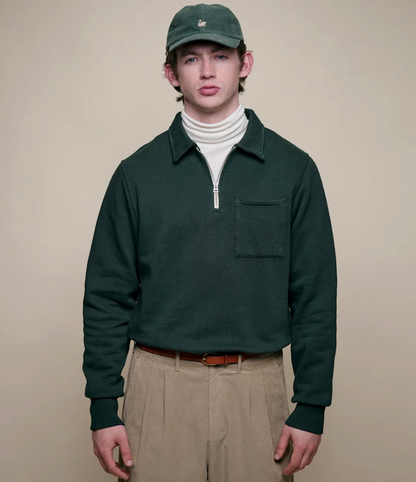 Person wearing a green pullover, beige pants, and a green cap on a beige background