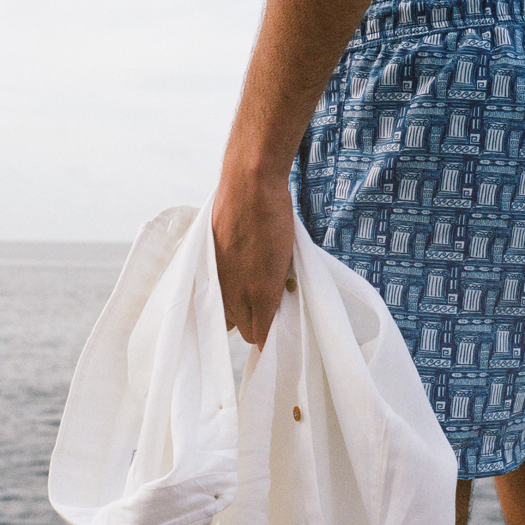 Person wearing a blue patterned shirt holding a white garment against a neutral background