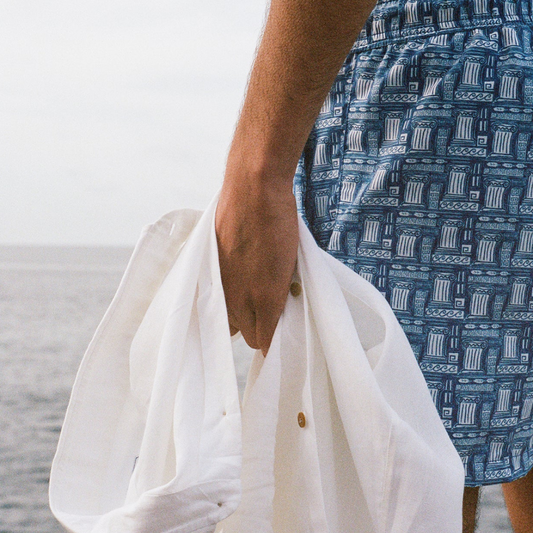 Person wearing a blue patterned shirt holding a white garment against a neutral background